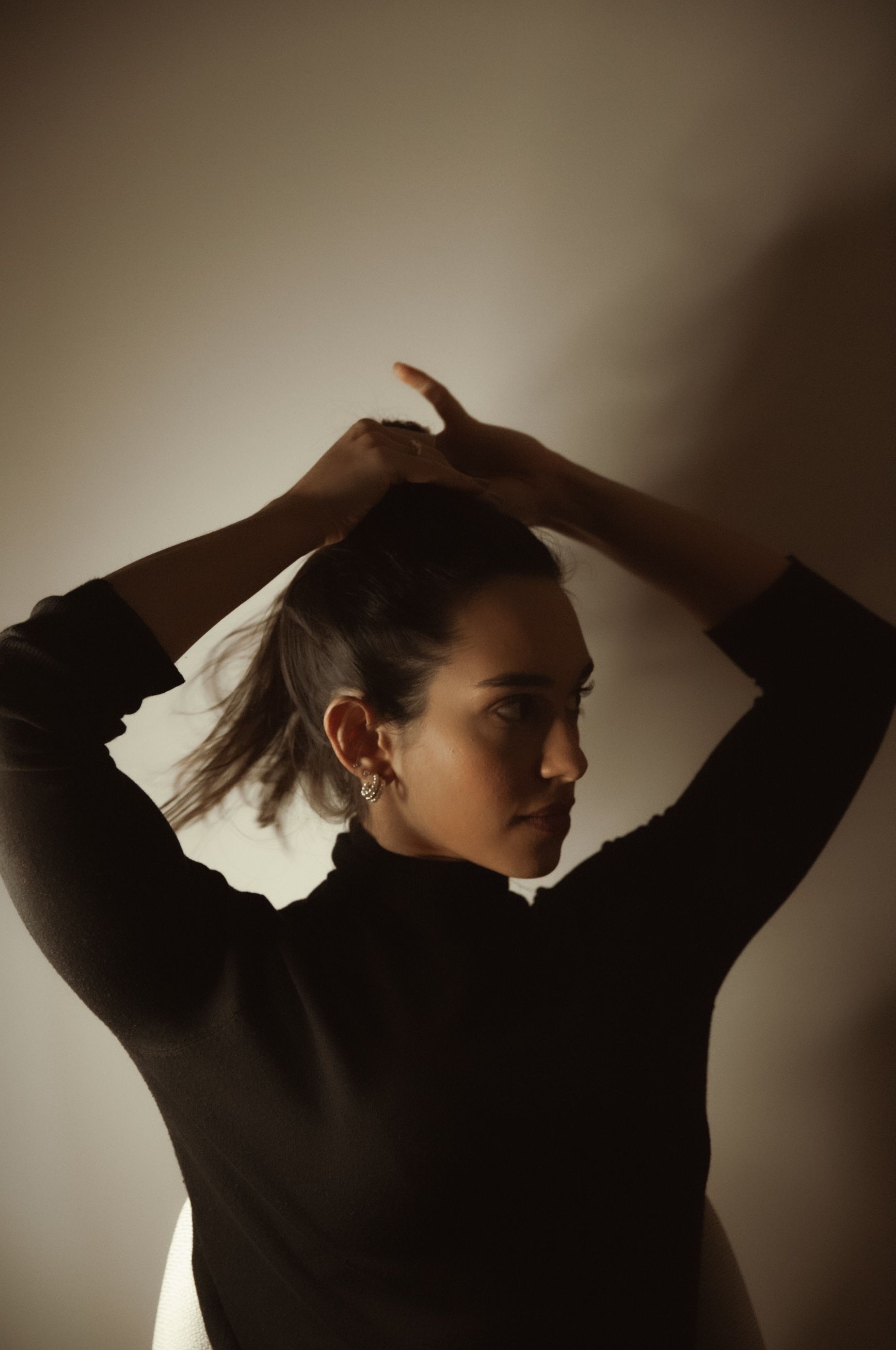 Retrato em contraluz de Bia ajustando o cabelo, em estúdio com luz dramática
